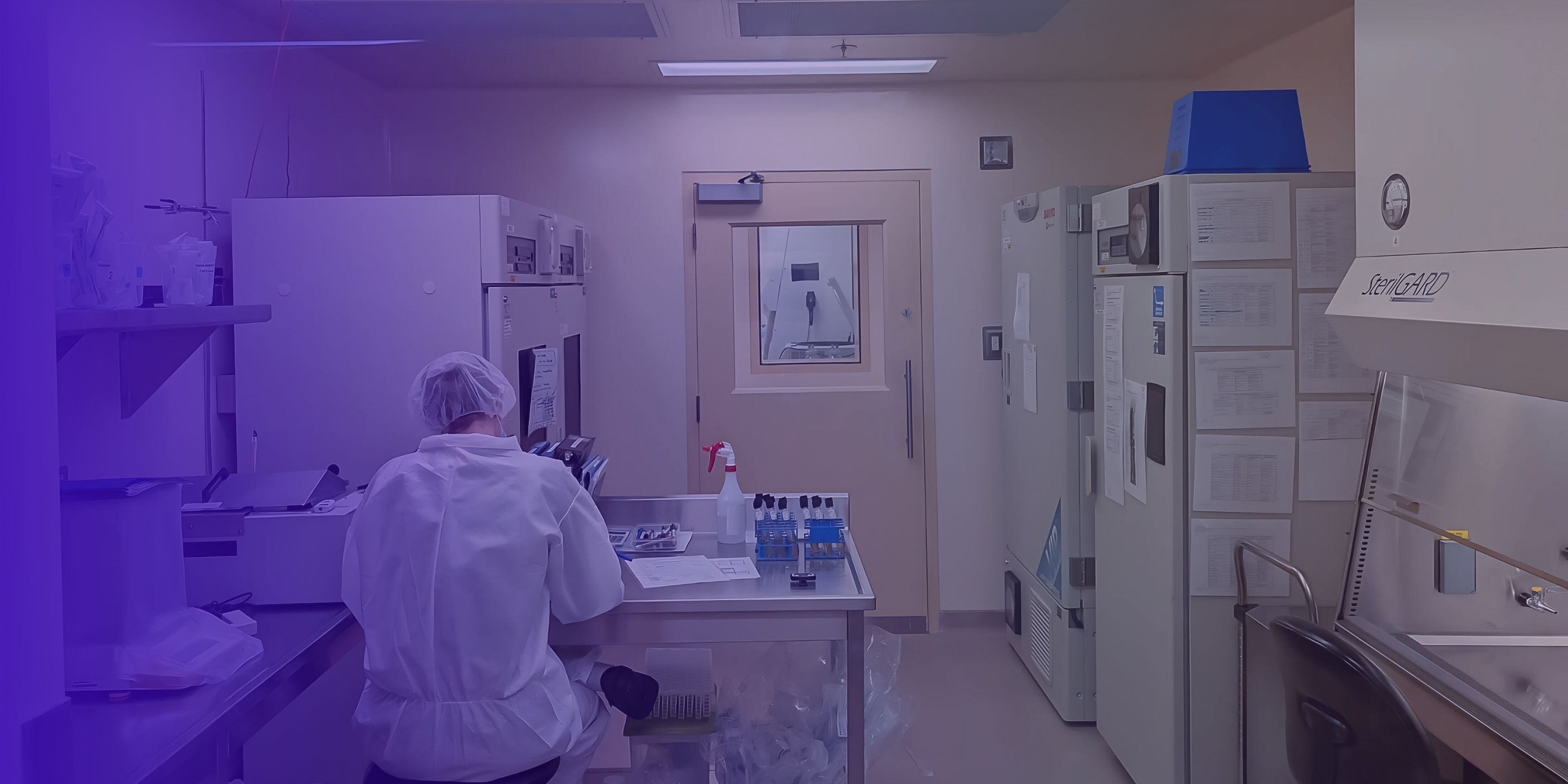 Technician in cleanroom operating a bioreactor in a controlled environment.