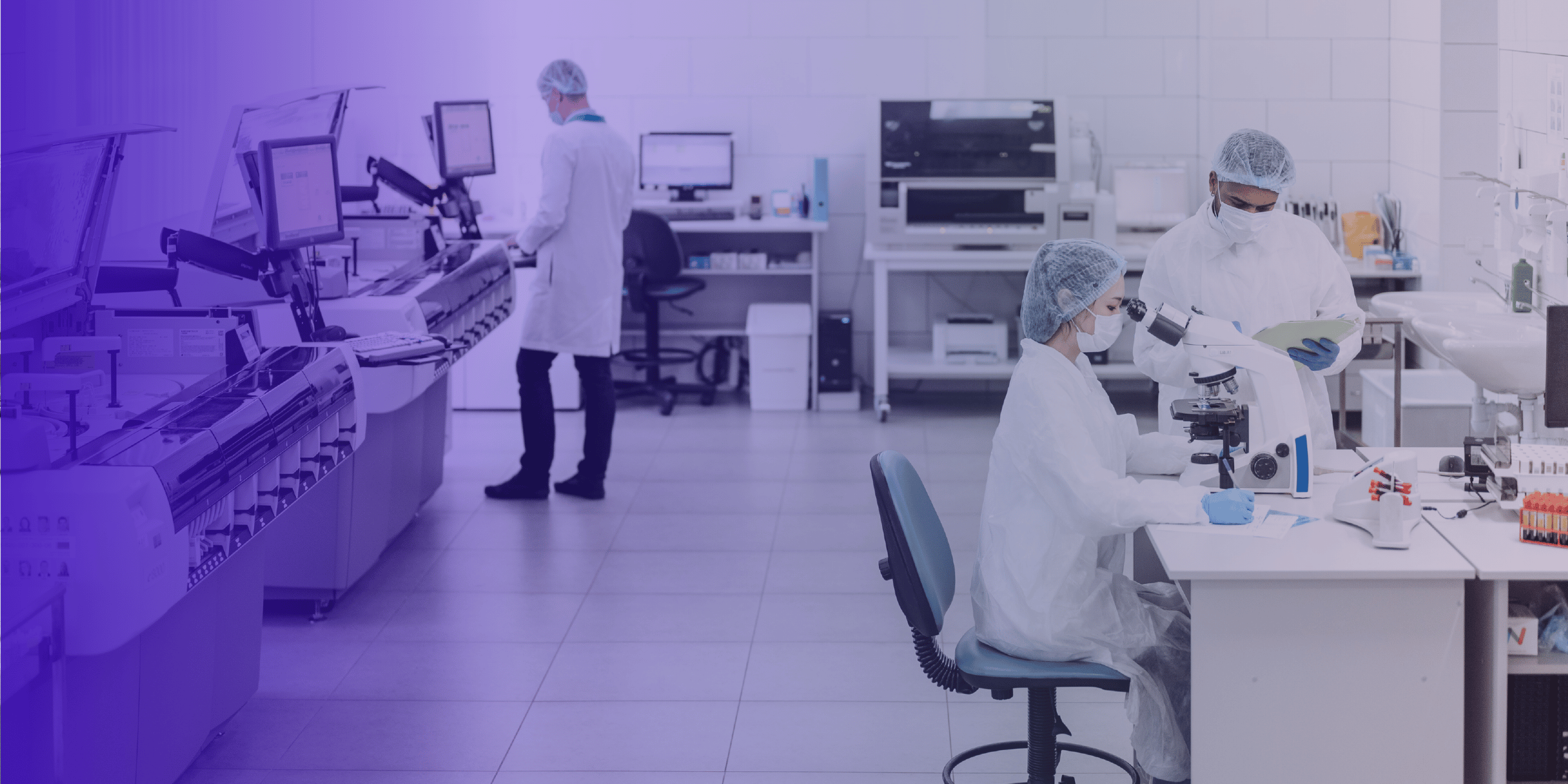 Researchers in pharmaceutical lab with microscopes and automated equipment.