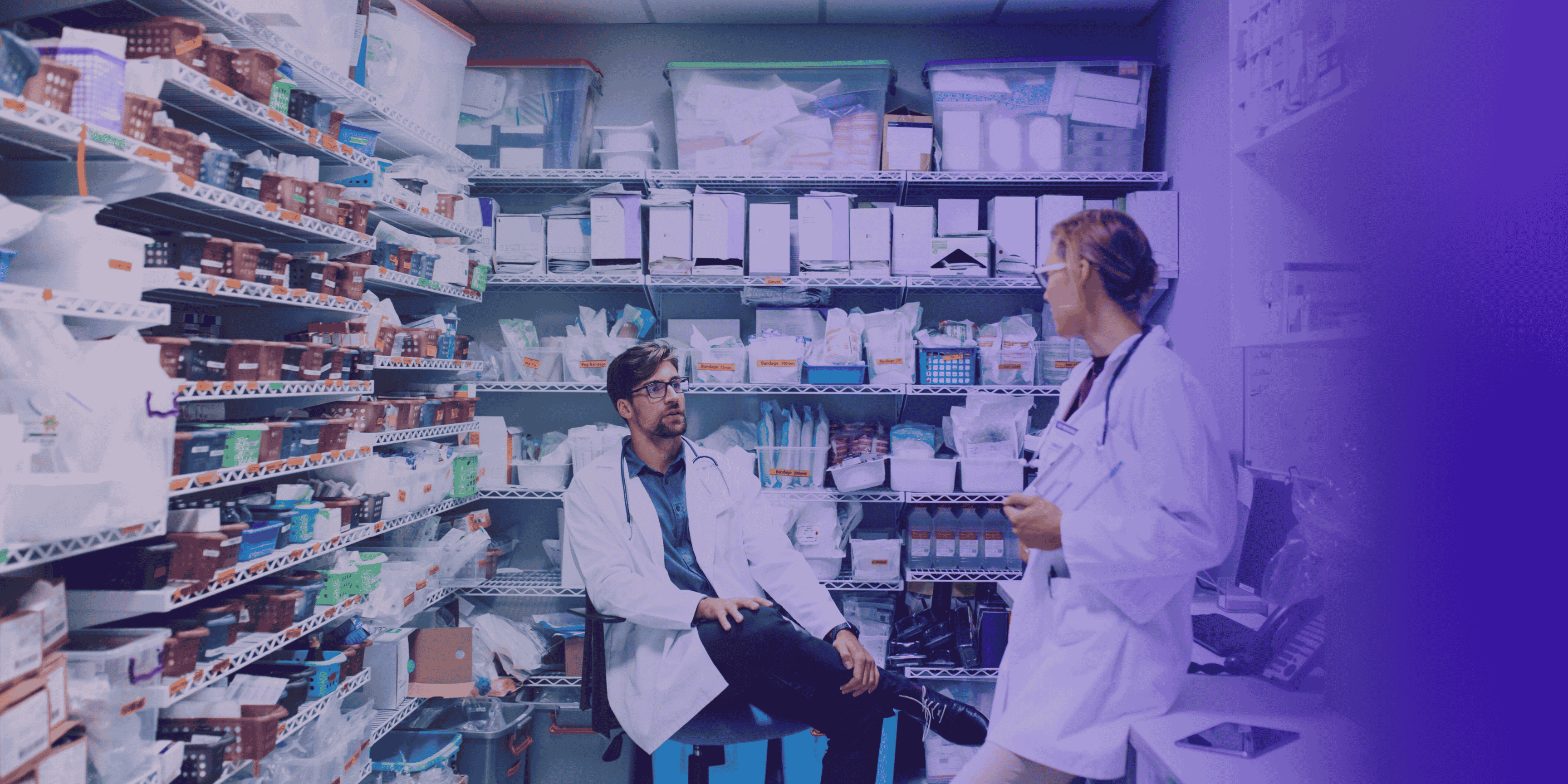 Two pharmacists talking in a well-stocked hospital pharmacy.