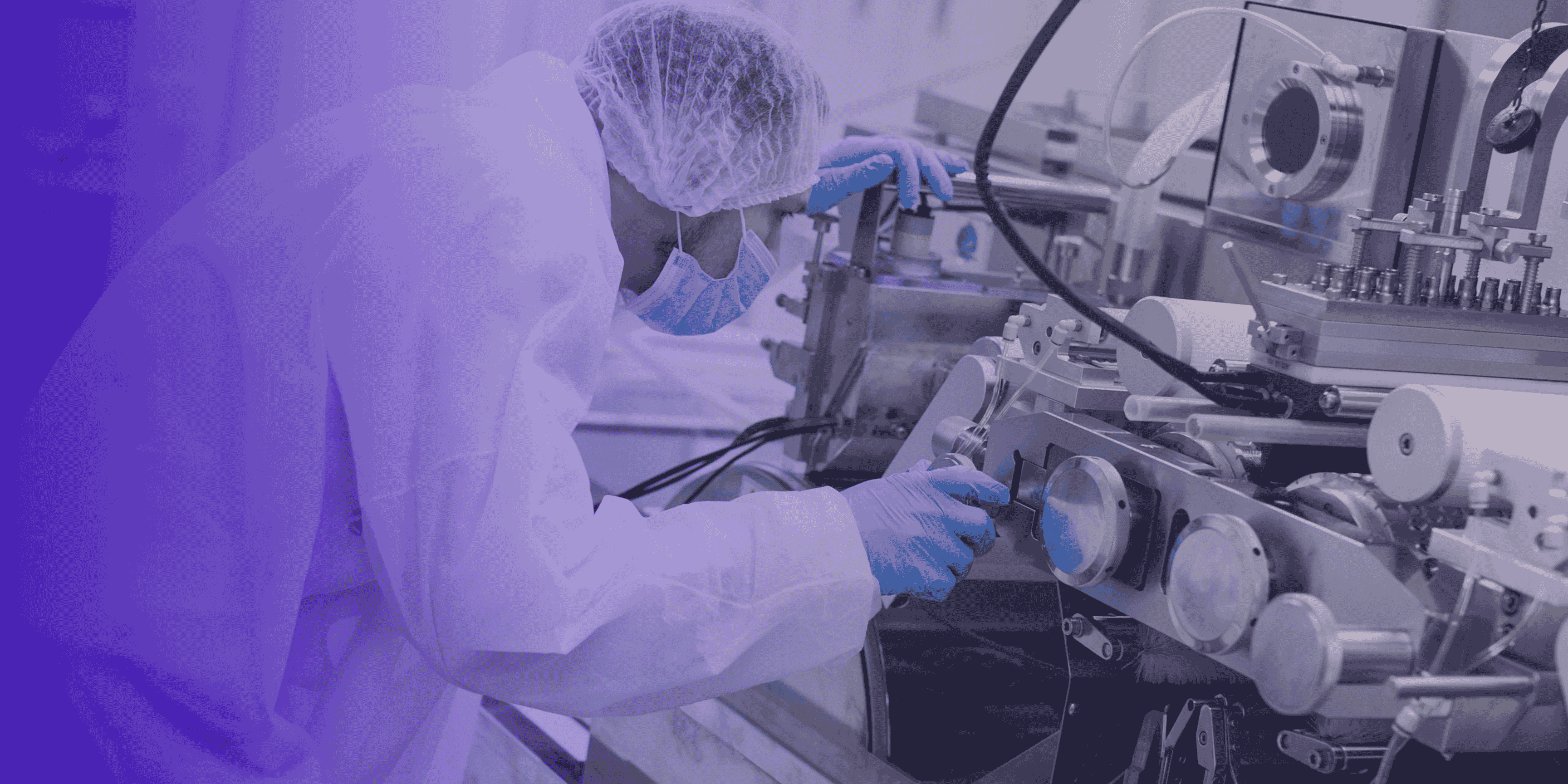 Technician in sterile gown inspecting a medical device manufacturing machine.