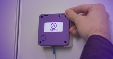 Hand adjusting a wall-mounted ATEK sensor to monitor critical parameters in a controlled environment.
