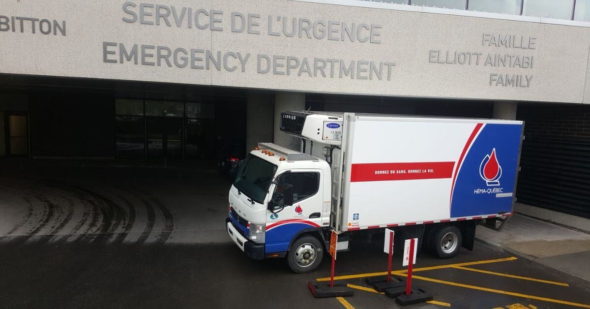 Camion de transport réfrigéré d’Héma-Québec stationné devant un service d’urgence, illustrant la chaîne du froid.
